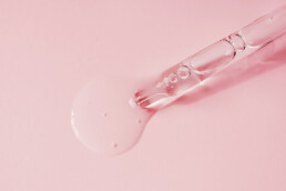 Pipette with fluid hyaluronic acid on pink background. Cosmetics and healthcare concept closeup. Dose of serum, retinol with air bubbles. Flat lay. Luxury beauty product presentation, macro